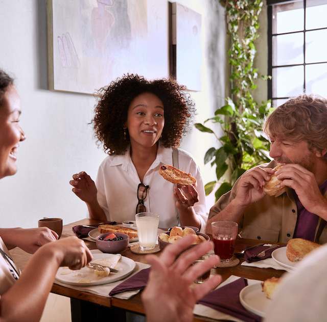 Imagem de quatro pessoas (dois homens e duas mulheres) sentados à mesa, comendo, sorrindo e conversando.