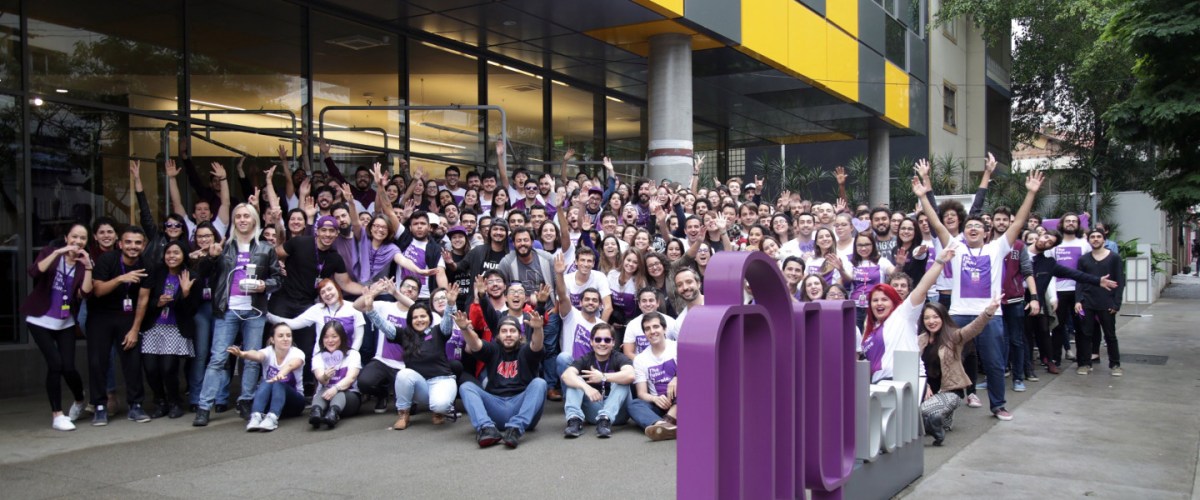 Grupo grande de funcionários do Nubank posando para foto na porta da empresa