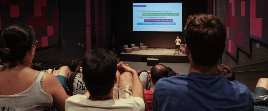 Encontro de Machine Learning no auditório do Nubank. A foto mostra os espectadores de costas e, ao fundo, um palestrante no palco