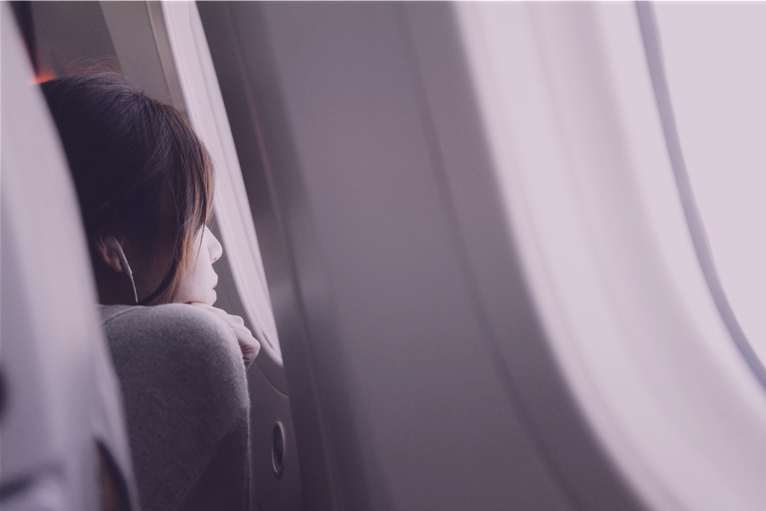 Jovem está com a testa quase encostada na janela do avião, olhando para fora