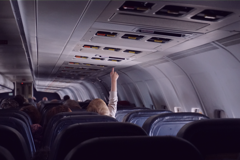 A foto mostra o interior de uma aeronave comercial. De costas, uma criança estica o dedo e tenta alcançar as luzes sobre a sua poltrona