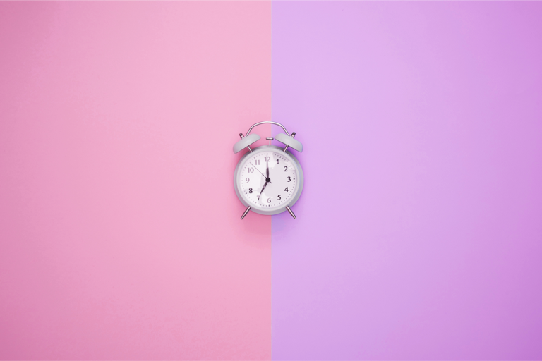 Relógio de ponteiro branco sobre um fundo metade rosa e metade roxo