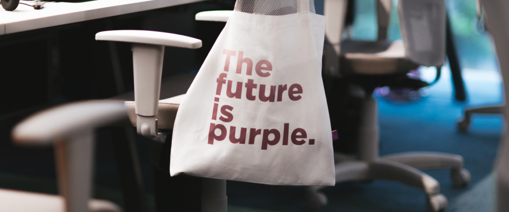 Foto mostra uma sacola branca com a estampa "The Future is Purple"(o Futuro é Roxo, em Português) pendurada em uma mesa