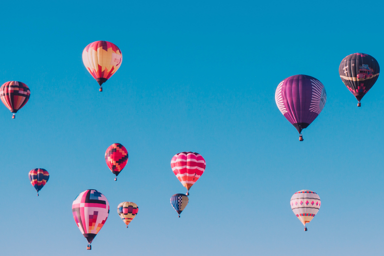 Balões de diversas cores e tamanhos voando em um céu azul.