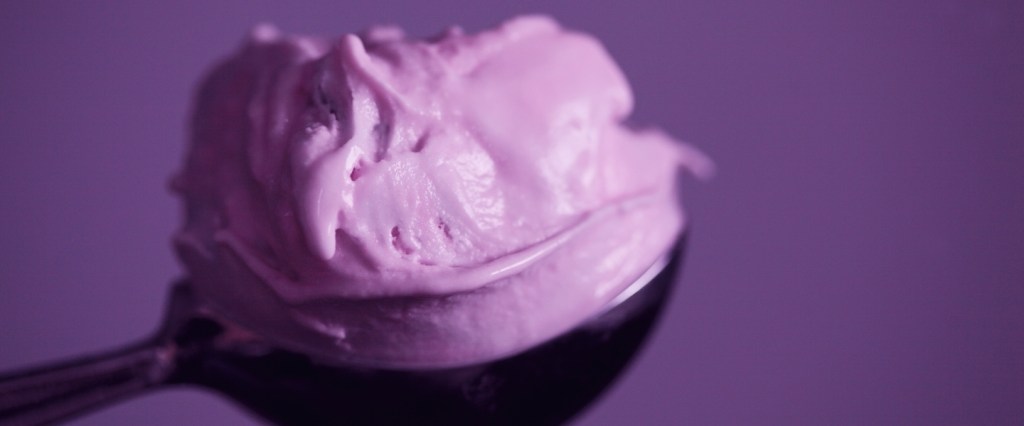 Em um fundo roxo, a imagem traz uma colher de metal com uma bola de sorvete lilás.