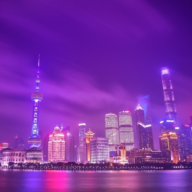 Skyline de Xangai a noite, com o céu roxo e reflexos dos prédios roxos e rosas na água