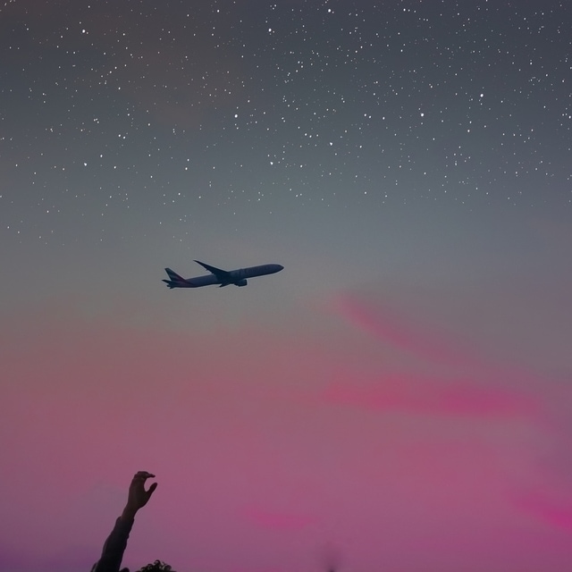 avião sobrevoando um céu de início de noite, com a parte de cima estrelada e a parte de baixo em tons de rosa