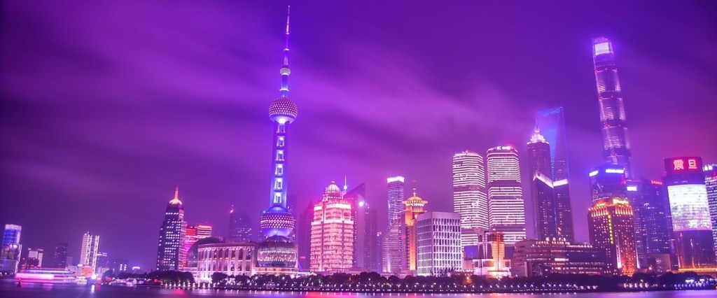 Skyline de Xangai a noite, com o céu roxo e reflexos dos prédios roxos e rosas na água