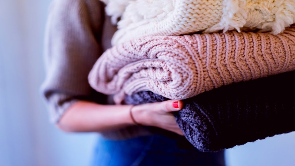 Mulher carregando uma pilha de malhas de tricô