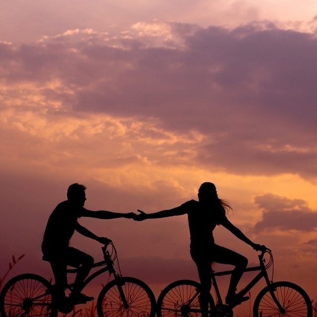 Seguro viagem: duas pessoas seguram mãos enquanto andam de bicicleta ao entardecer