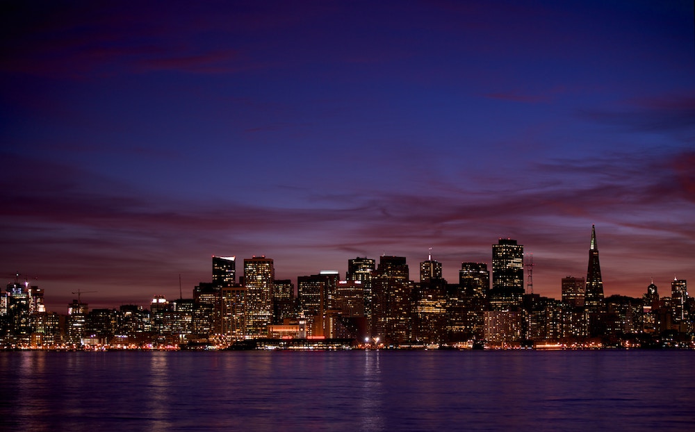 Foto de uma cidade à noite, com diversos arranha céus iluminados.