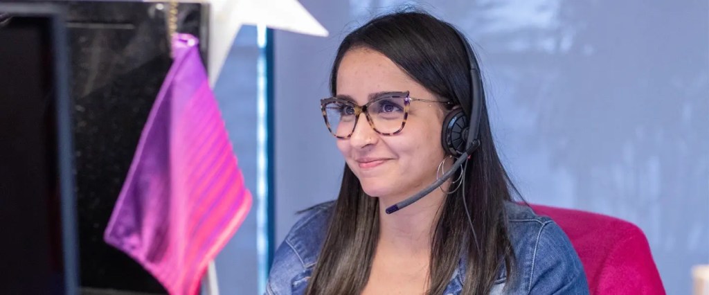 Vagas Nubank: jovem sentada em frente ao computador, de óculos, sorrindo