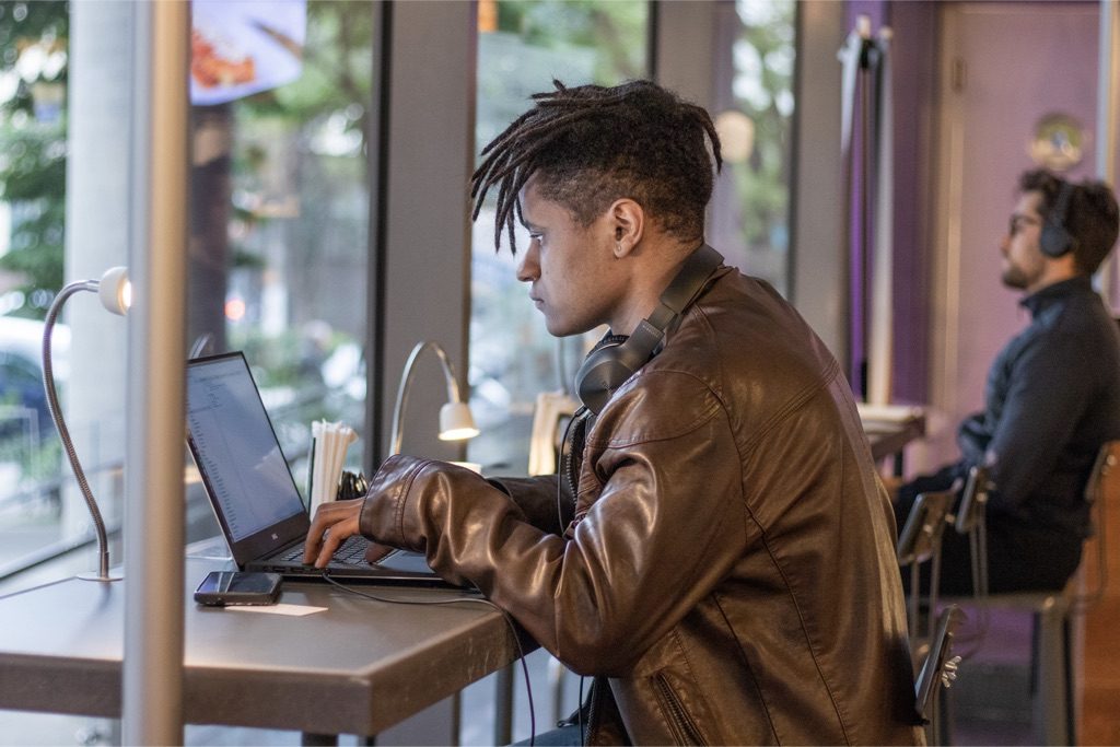 Vagas Nubank: jovem sentado em frente ao computador, trabalhando em um café