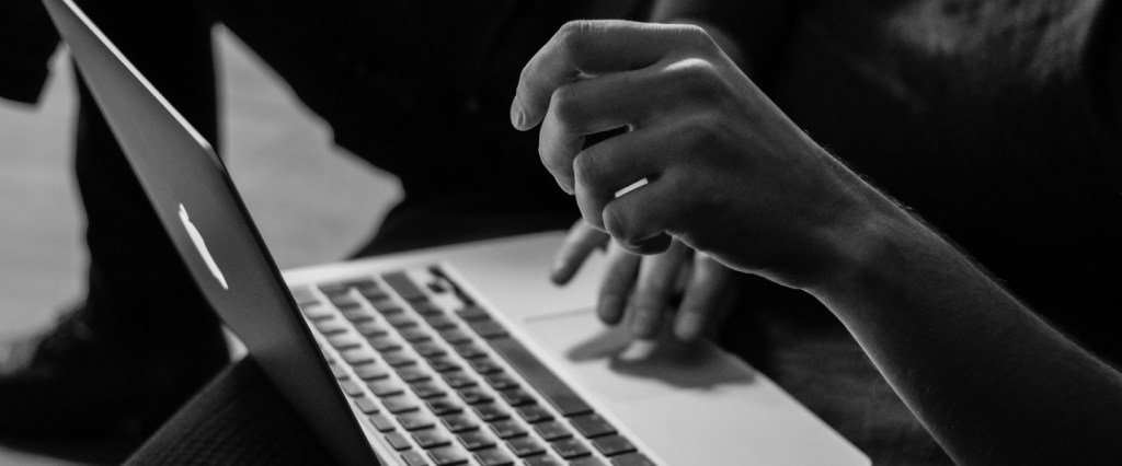 Imagem em preto e branco com a mão de mulher mexendo em um notebook.