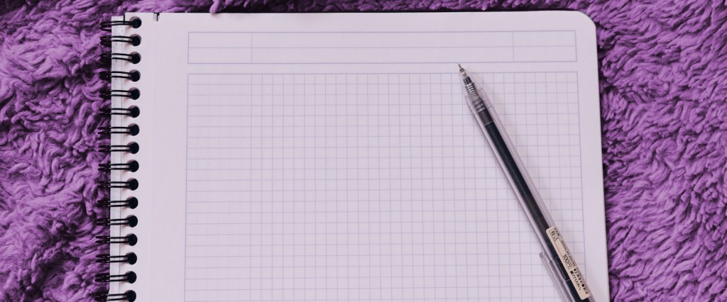Caderno quadriculado em branco com uma caneta em cima sobre um tapete roxo