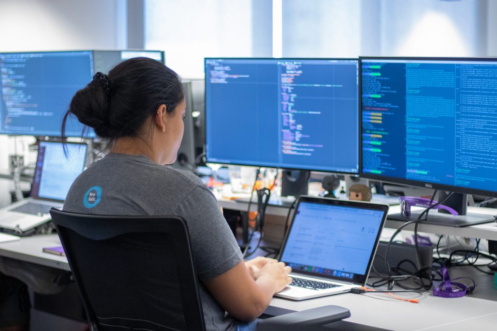 Uma mulher trabalha com código de programação em três telas de computador.