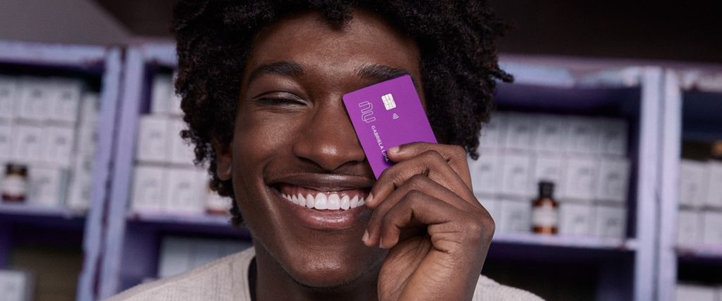 Nubank milhas Smiles: homem sorrindo segurando um cartão de crédito Nubank na frente do rosto