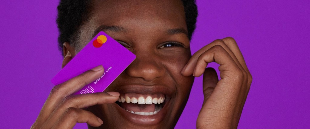 Antecipar Parcela: foto mostra jovem com cartão de crédito nubank em frente ao rosto e sorrindo