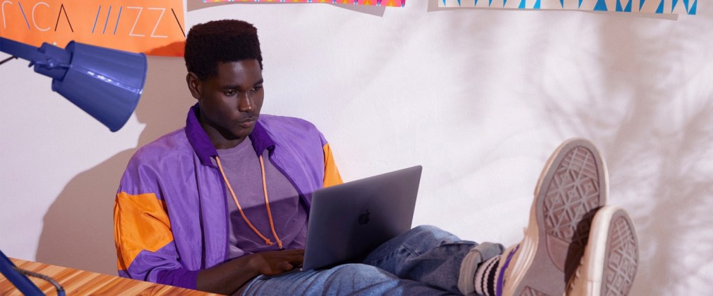 Web app: veja tudo o que dá pra fazer pelo site do Nubank: Imagem mostra um jovem de jaqueta roxa sentado, com os pés em cima da mesa, e um laptop no colo