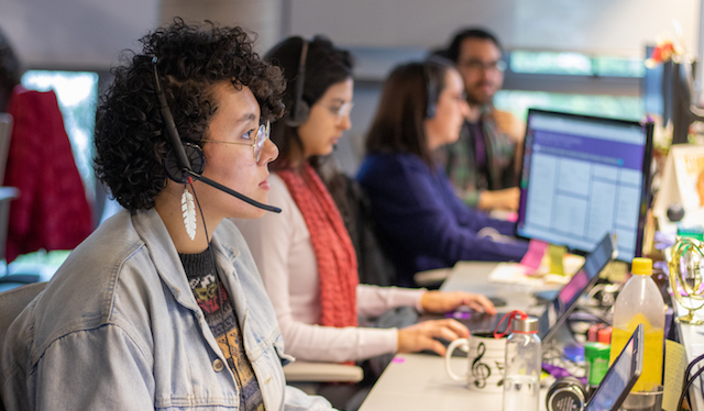 Carreiras por trás da conta do Nubank: foto de quatro pessoas com fones de ouvido com microfone trabalhando numa mesa compartilhada.