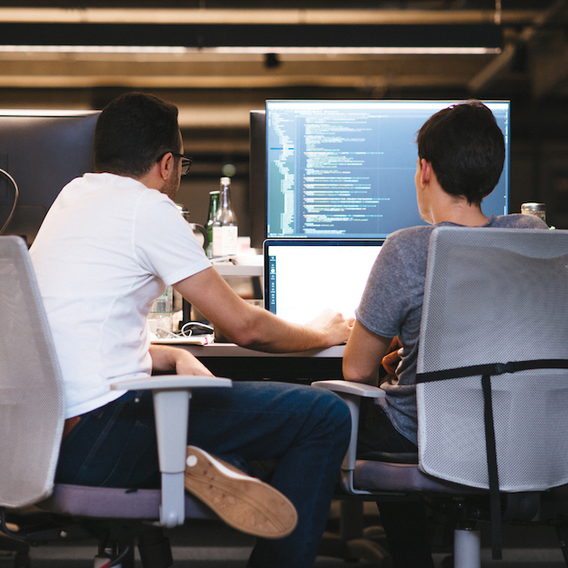 Data Science: dois homens sentados olhando para um computador. Na segunda tela, um programa de código de programação.