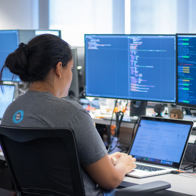 O que é Clojure: foto de uma mulher trabalhando com um notebook e dois monitores que exibem códigos de programação.