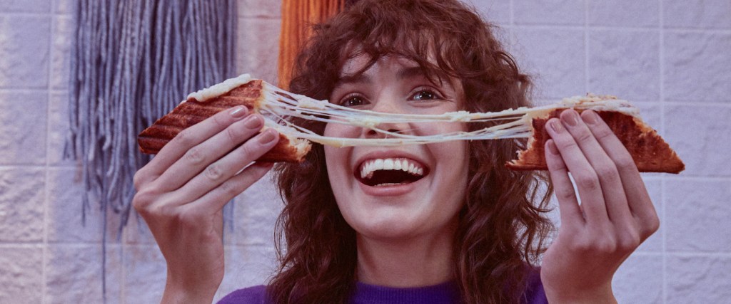 mulher sorrindo com queijo quente na mão