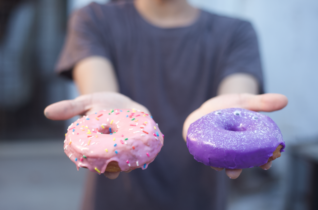 Mãos do cliente segurandos dois donuts, um rosa e um roxo