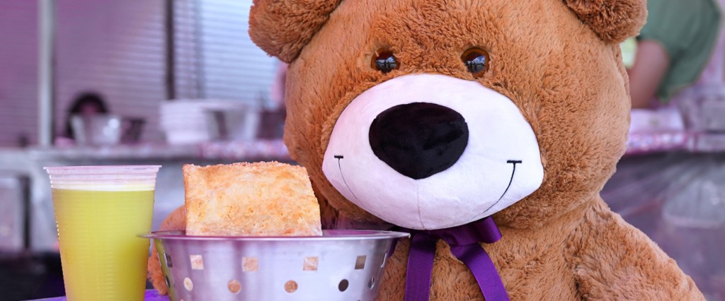TED: o Urso TED do Nubank em uma feira de rua comendo pastel e tomando caldo de cana.