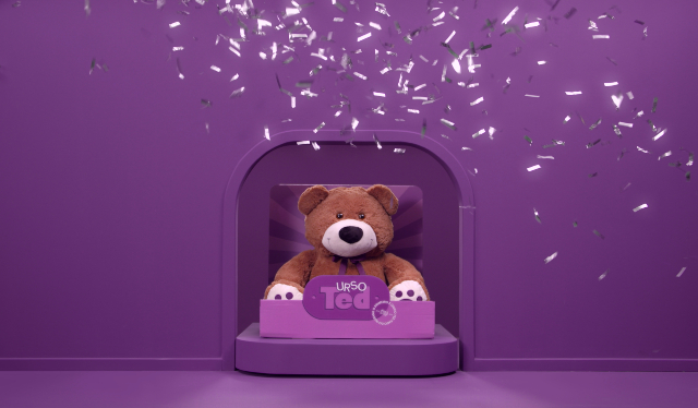 TED Bear: ursinho do Nubank em uma caixa e cenário roxo com chuva de prata caindo sobre ele