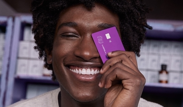 Homem sorrindo segurando um cartão de crédito Nubank na frente do rosto
