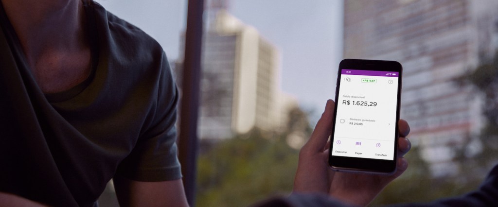 App Nubank: pessoa segurando celular com o aplicativo na tela