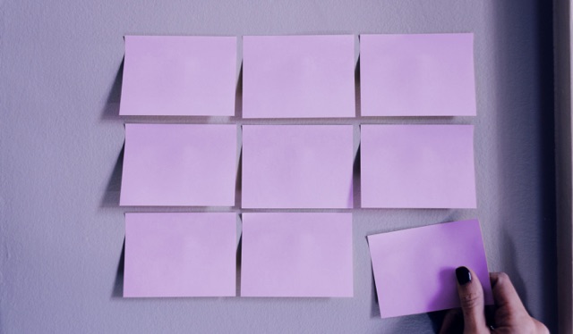 MVP: imagem de 9 post its roxos em grupos de 3 colados em uma parede, com uma mão retirando o mais abaixo