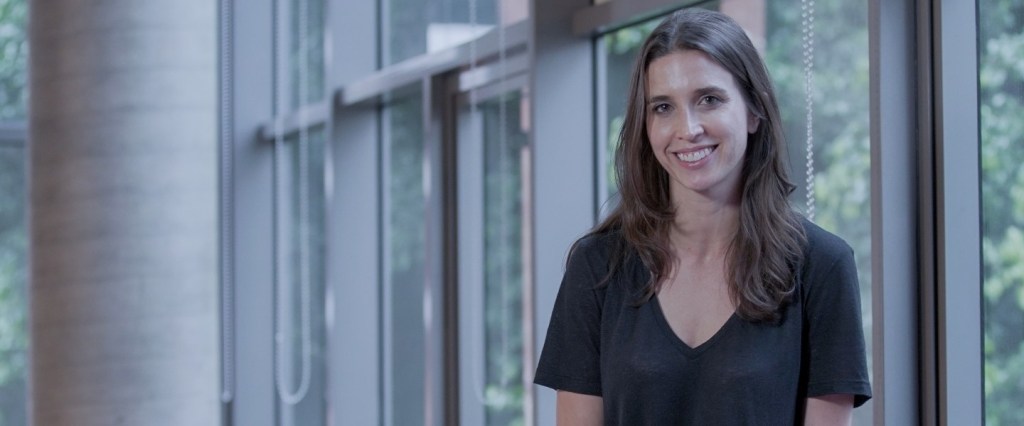 Product Manager: Foto de Aly sentada sorrindo, usando uma camiseta preta