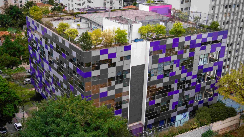 Na imagem aparece o escritório do Nubank em uma foto aérea, cercado por árvores e com janelas roxas