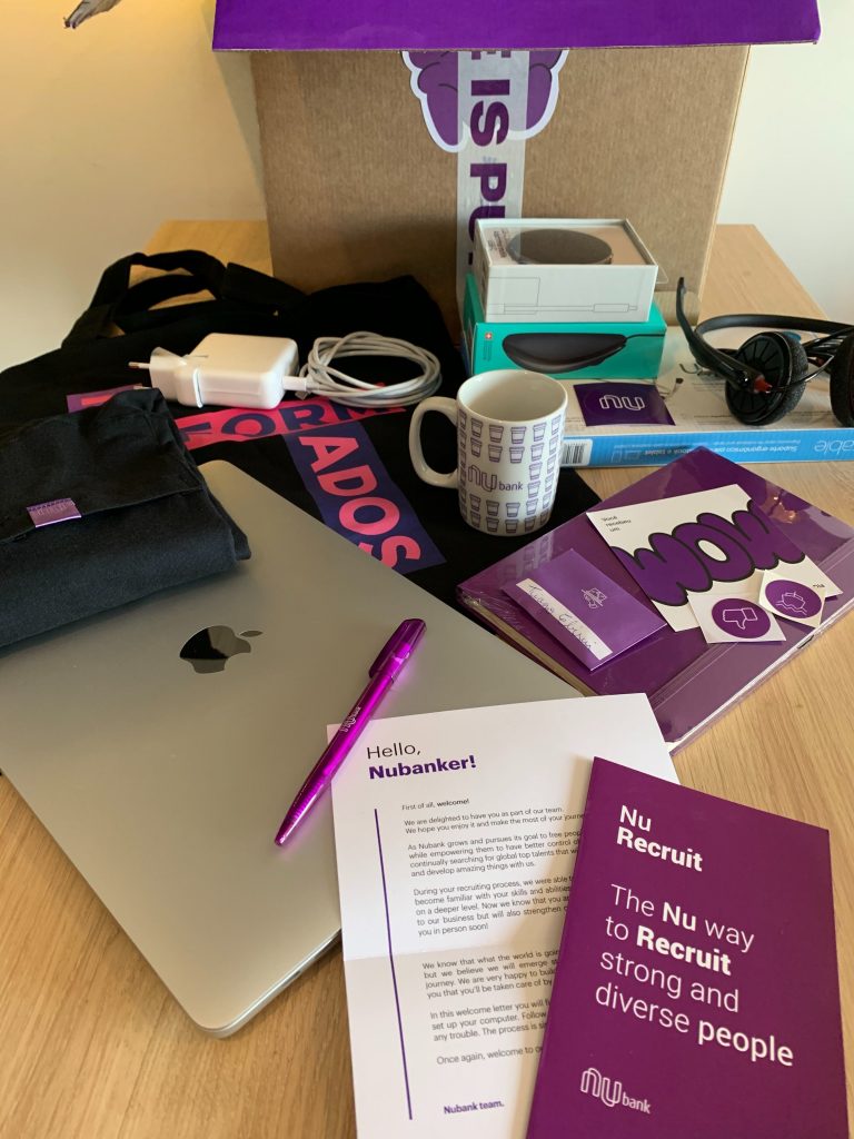 Nubank welcome kit: a computer and purple items, such as a pen, a letter and mug.