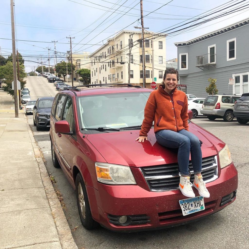 Imagem de Demi sentada sobre o capô de um carro vermelho estacionado na rua