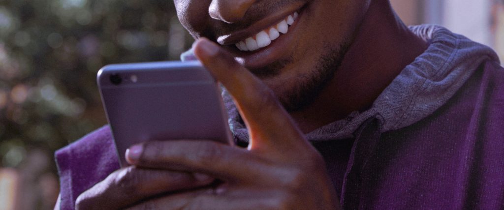 Resgate Planejado Nubank: Jovem vestindo moletom roxo segura um celular em frente ao seu rosto enquanto sorri.