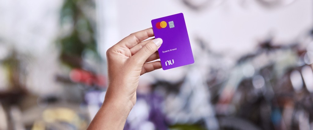 Prêmio iBest 2023: imagem mostra, em primeiro plano, a mão de uma pessoa branca segurando cartão do Nubank com o nome 