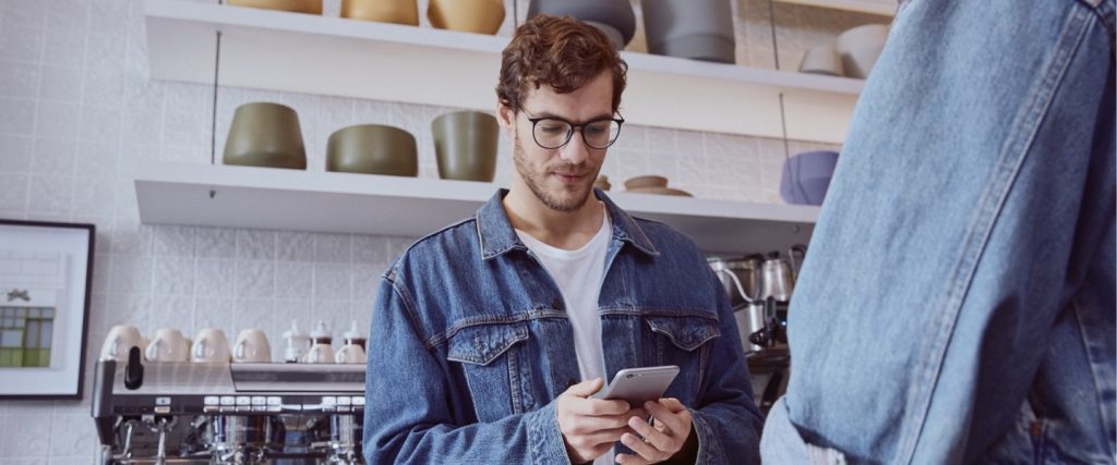 Para que serve o Pix: imagem mostra jovem de óculos e jaqueta jeans, atrás de um balcão de café, olhando para o telefone
