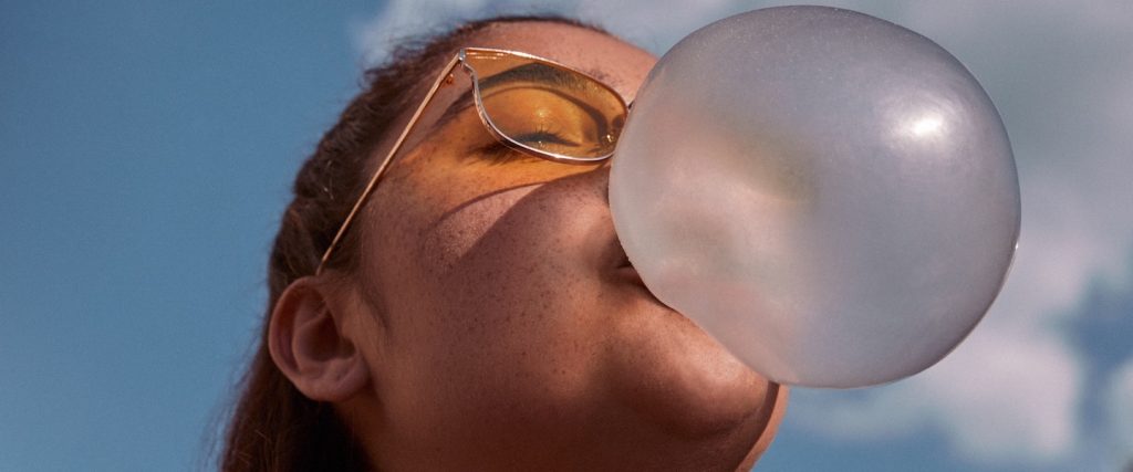 Pix Nubank: mulher de óculos de lente amarela olhando pra cima e fazendo uma bola de chiclete
