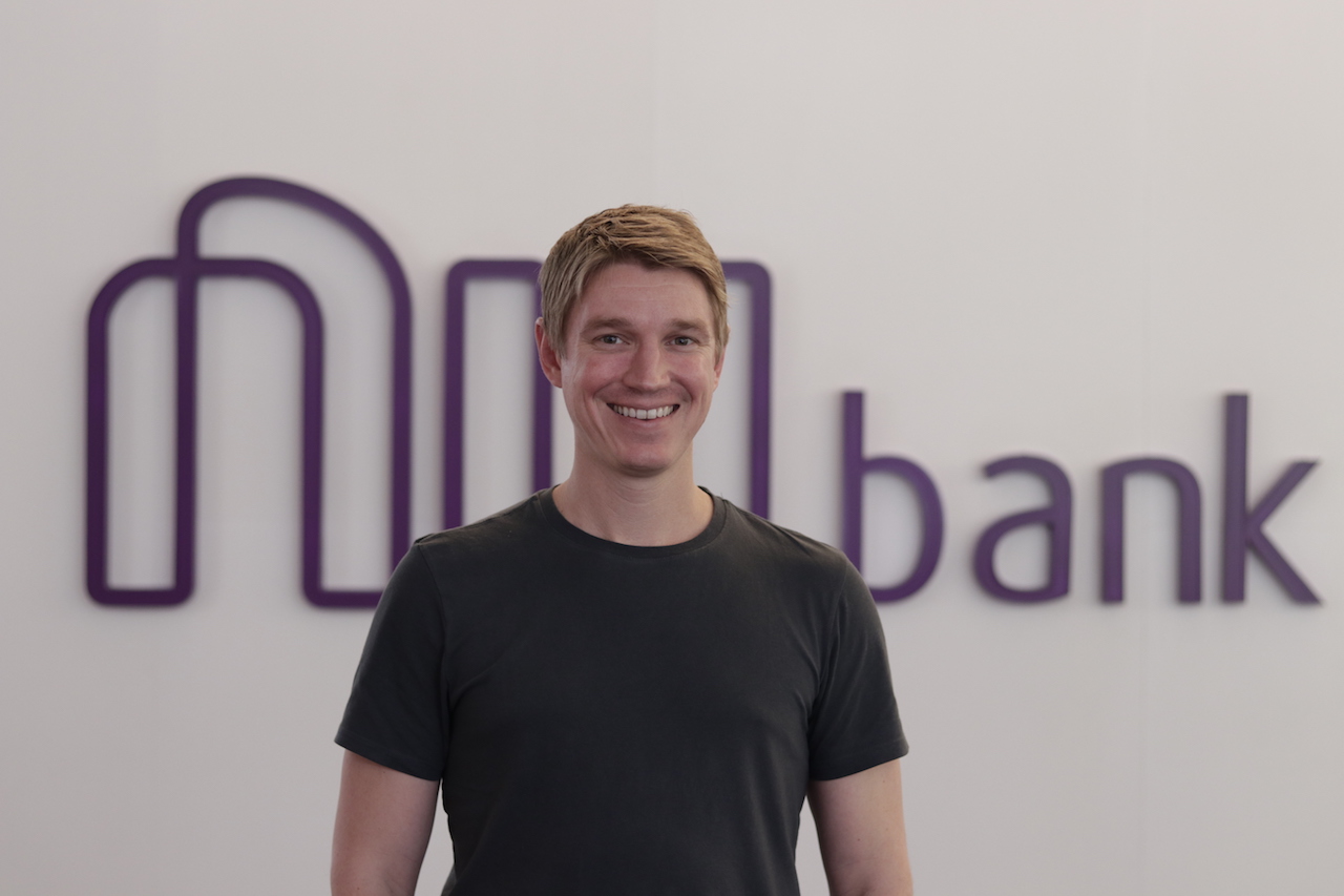 Fotografia de Edward Wible em frente ao logo do Nubank