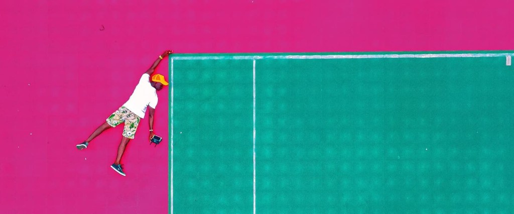 Como funciona o MEI: no fundo rosa, ilustração de um homem se segurando na ponta de uma quadra de tênis