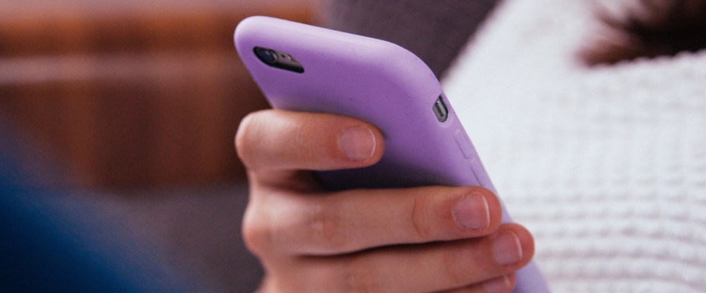 Prova de vida digital: Mão de jovem segurando um telefone com capa roxa