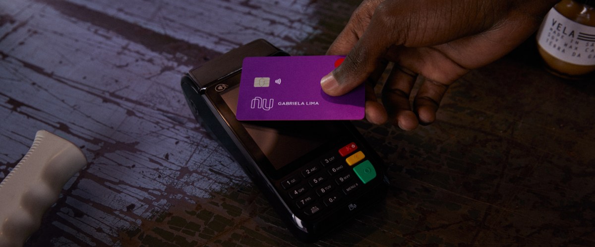 Contactless na quarentena: Uma mão segurando o cartão Nubank e aproximando da maquininha.