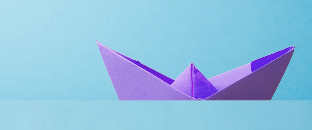 Compras com viagem aumentam na Cyber Monday, aponta Nubank: Imagem de um barquinho de papel roxo em um fundo azul claro