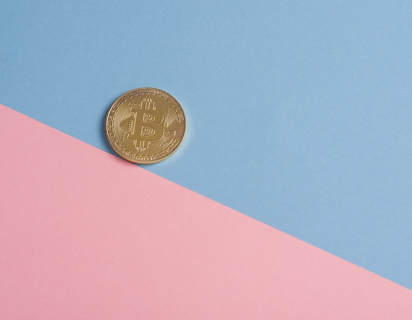 Bitcoin: uma moeda dourada de bitcoin sobre uma superfície azul e rosa