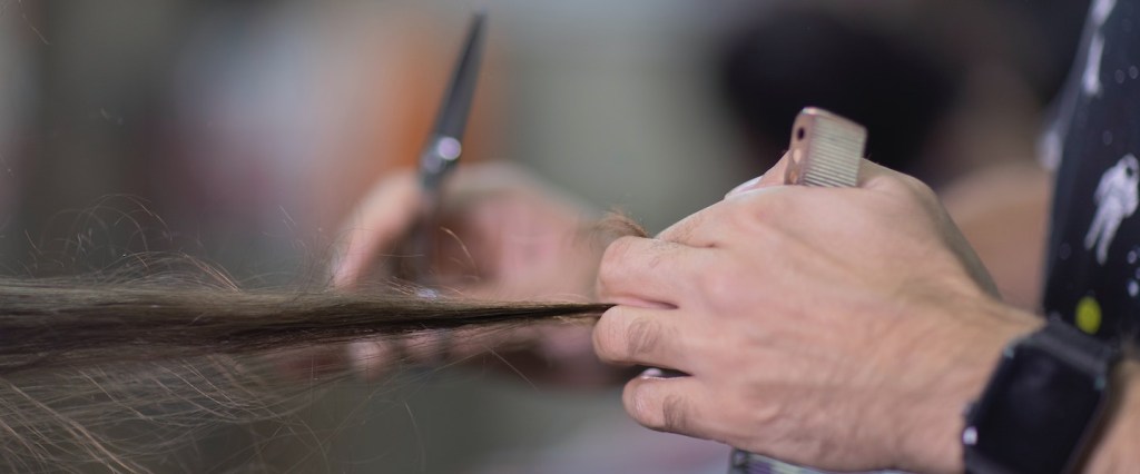 Década do MEI: fotografia de uma pessoa cortando um cabelo cumprido. Uma mão segura o cabelo e outra segura a tesoura.