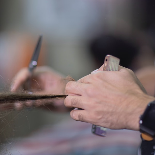Década do MEI: fotografia de uma pessoa cortando um cabelo cumprido. Uma mão segura o cabelo e outra segura a tesoura.