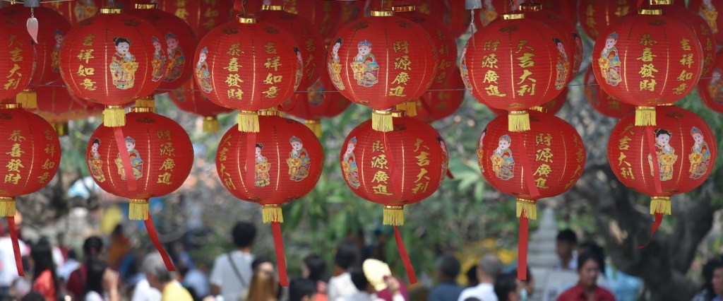 Imagem de lanternas chinesas penduradas com várias pessoas andando embaixo